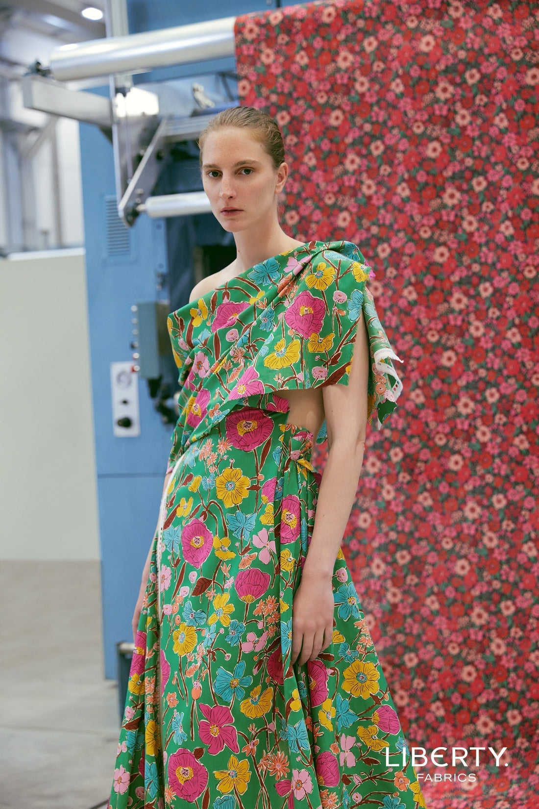 Model wearing a vibrant Liberty Fabrics Tana Lawn™ cotton dress in front of a floral fabric backdrop at Liberty Fabrics.