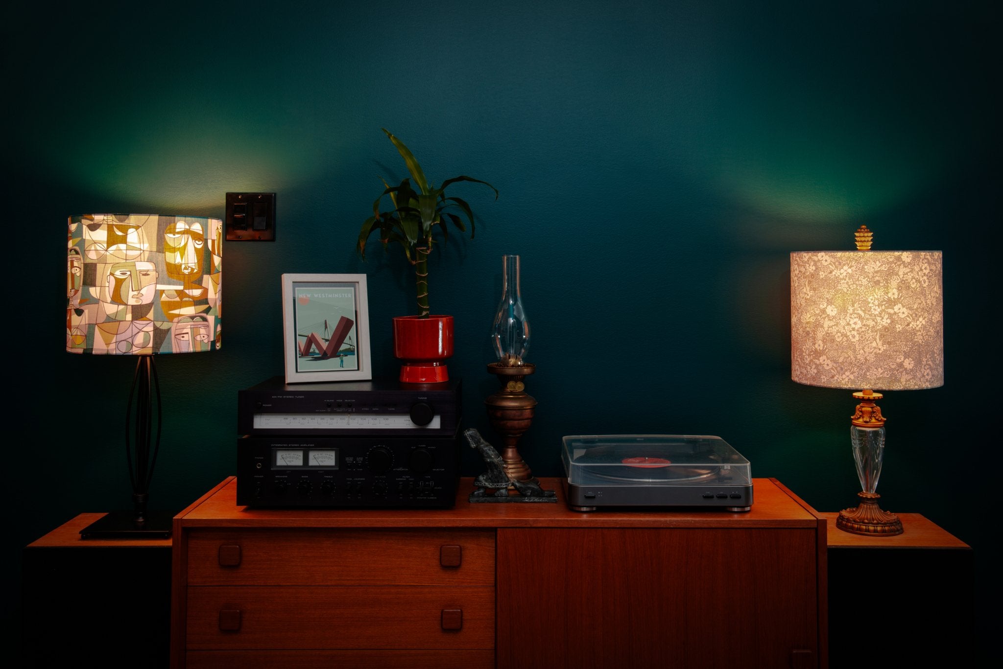 Vintage record player on a wooden cabinet with two Kikiwi lampshades against a dark teal wall.