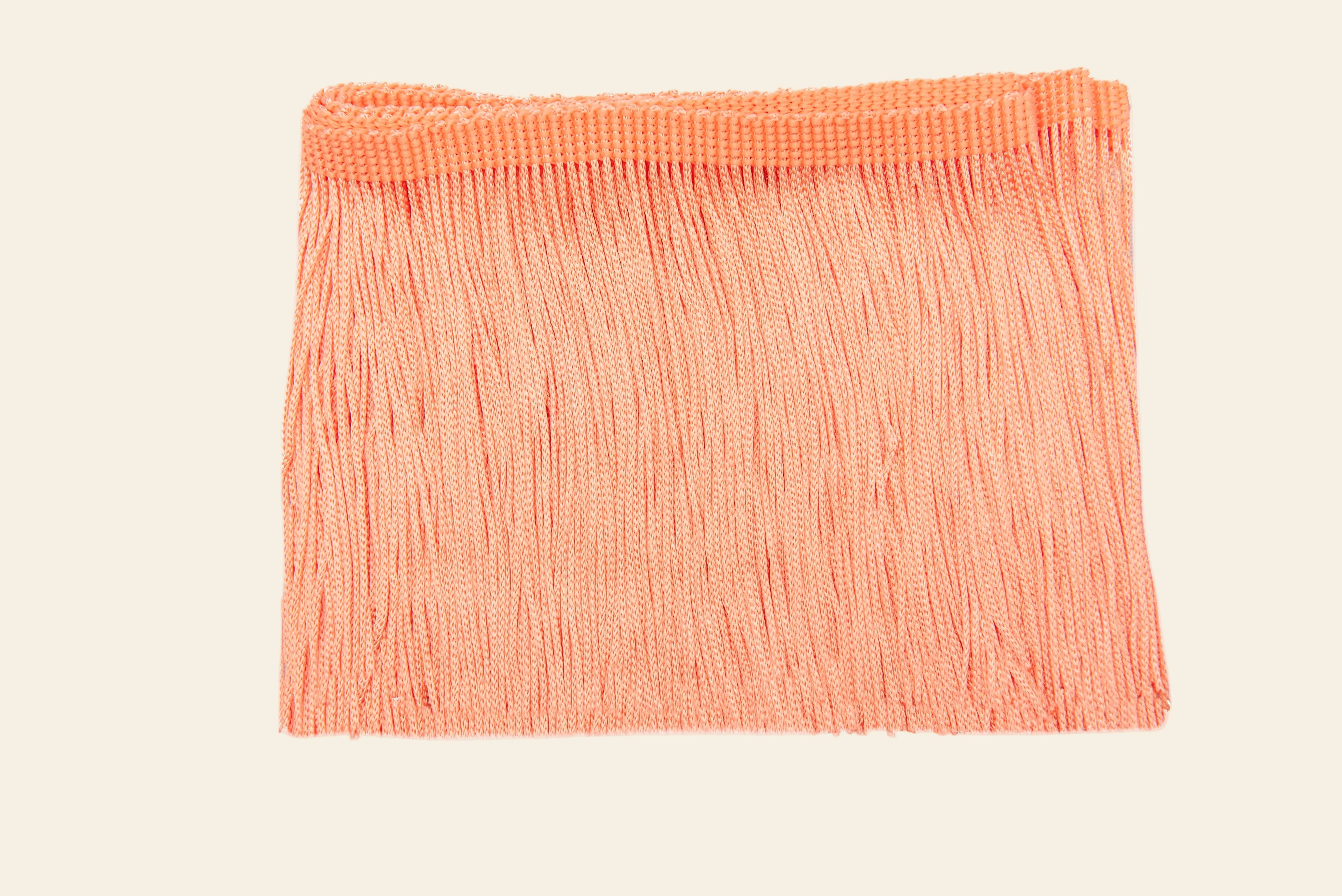 Coral colored peach fringe trim fabric on a white background