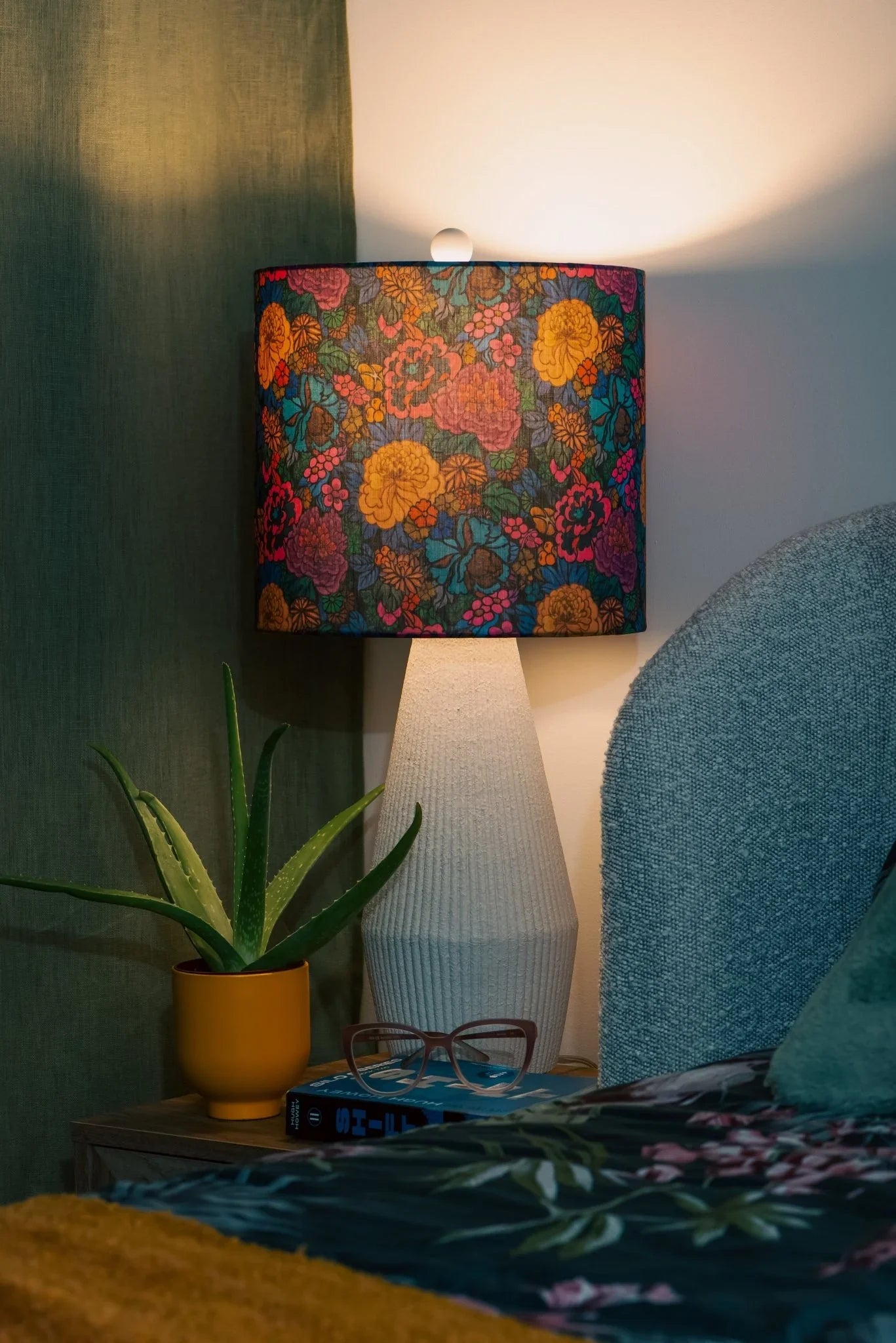 Handmade Sakura drum lampshade in Liberty Heritage Garden cotton, glowing on a wooden bedside table in a cozy bedroom