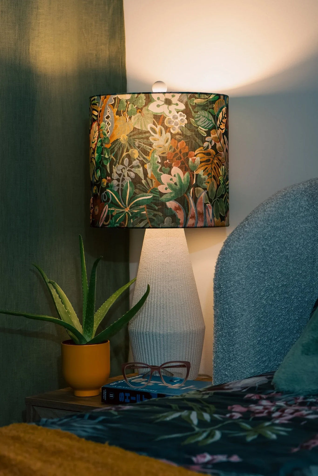 Jungle Trip Liberty fabric drum lampshade on a wooden nightstand, casting warm light in a tropical bedroom