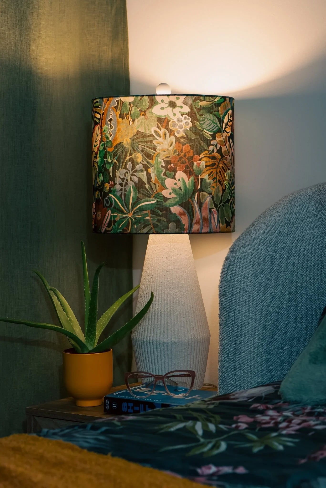 Jungle Trip Liberty fabric drum lampshade on a wooden nightstand, casting warm light in a tropical bedroom
